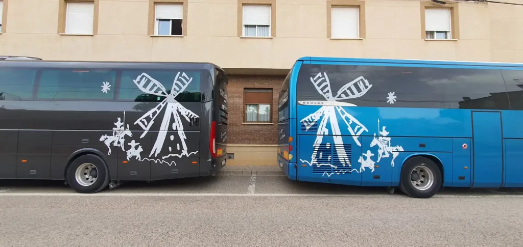 Dos autobuses de Viajes Claira, uno negro y otro azul, con ilustraciones de Don Quijote y molinos de viento, aparcados lado a lado antes de una excursión organizada por Castilla-La Mancha.