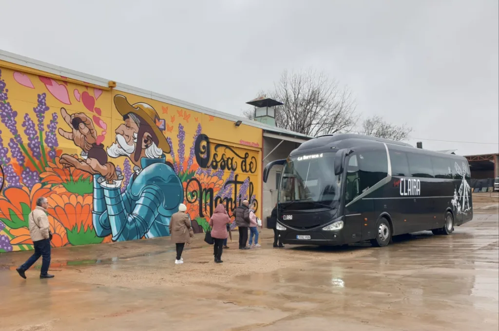 Grupo de viajeros subiendo al autobús de Viajes Claira frente al mural turístico de Ossa de Montiel, en una excursión organizada por La Mancha.