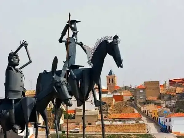 Estatua metálica de Don Quijote y Sancho Panza a caballo con el pueblo al fondo.