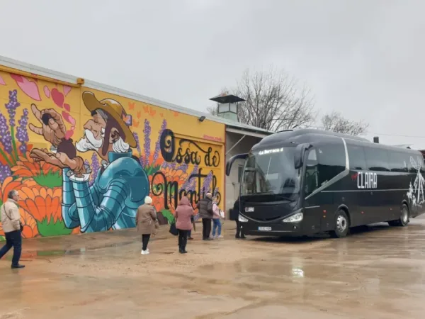 Grupo de viajeros subiendo al autobús de Viajes Claira frente al mural turístico de Ossa de Montiel, en una excursión organizada por La Mancha.