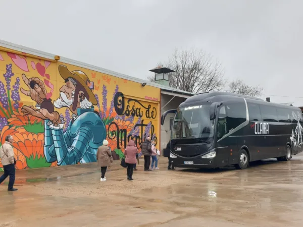 Grupo de viajeros subiendo al autobús de Viajes Claira frente al mural turístico de Ossa de Montiel, en una excursión organizada por La Mancha.