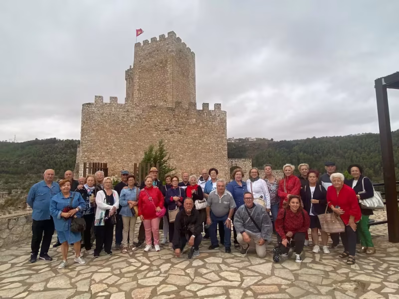 Jubilados posando junto a la torre de un castillo en un viaje organizado para mayores